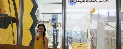 Payton Barnwell beside the James Webb Space Telescope’s gold mirror segments, behind glass.