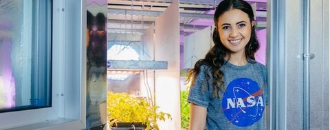 Payton Barnwell in a NASA shirt at the door of a plant growth chamber.