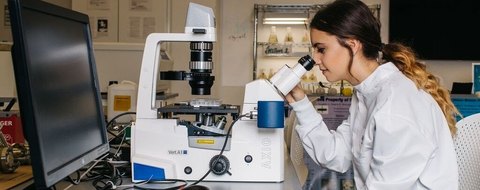 Payton Barnwell at a microscope in a Florida Poly lab, in a white coat.